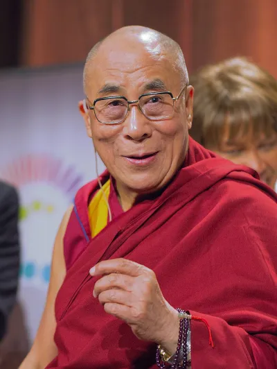 Der Dalai Lama trägt das gewohnte rote Gewand. Aus dem Brustbild heraus scheint er den Betrachter amüsiert und etwas erstaunt anzulächeln.