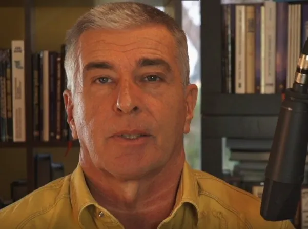 Kleines Standbild aus einem Video von Jo Conrad im gelben Hemd, im Hintergrund Bücherregale.
