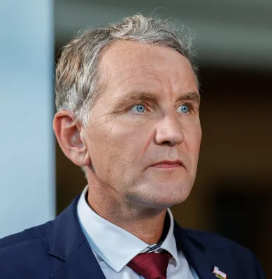 Björn Höcke trägt eine dunkelblaue Anzugjacke, Oberhemd und einen roten Schlips und blickt konzentriert nach rechts aus dem Bild heraus.