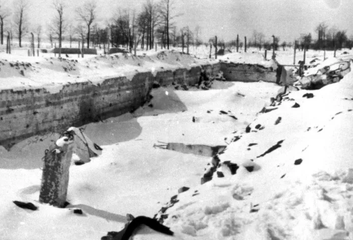 Eine schneebedeckte Grube, in der Grube undam Rand erkennt man einige Trümmerstücke.