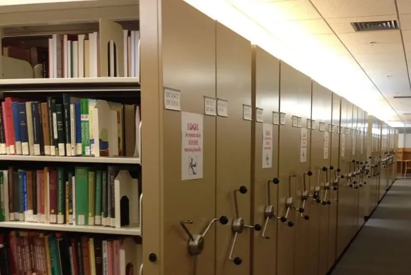 Links die umfangreiche Rollregalanlage einer Universitätsbibliothek, rechts daneben ein Gang.