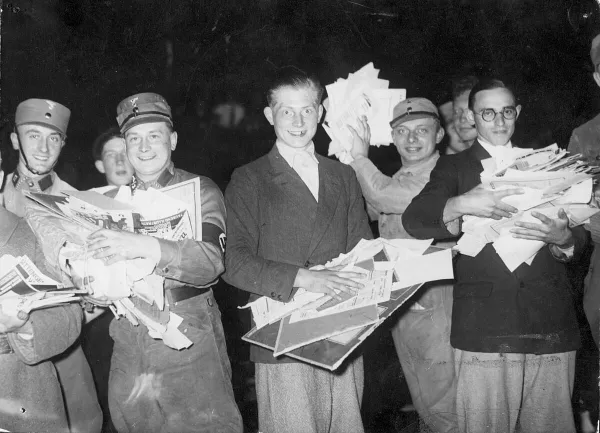 Fröhlich lachende junge Männer in SA-Uniformen zeigen dem Fotografen Druckwerke, die sie gleich verbrennen wollen.