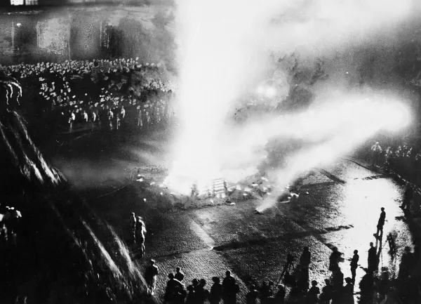 Blick von oben auf den Opernplatz. Ein riesiges Feuer in der Mitte, ringsherum stehen Menschen und schauen zu, es sind viele Uniformierte zu erkennen.