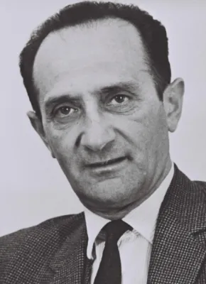 Ein schwarzweißes Brustbild, der Mann mit zurückweichendem Haaransatz und zurückgekämmtem dunklem Haar trägt Anzugjacke, Hemd und Krawatte.